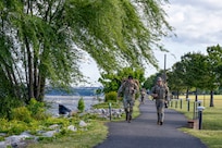 Two Airmen approach marching on a paved path next to the river.