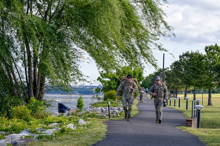 Two Airmen approach marching on a paved path next to the river.