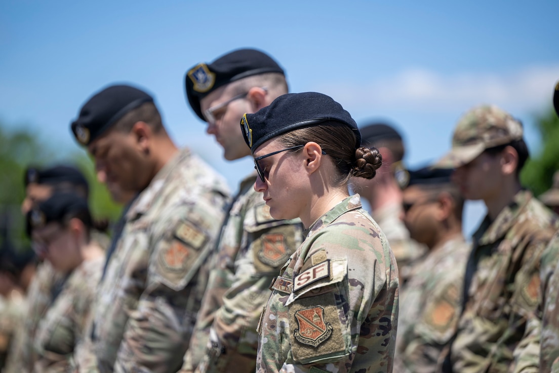 An Airman facing left and wearing a black beret bows her head with others doing the same behind her.