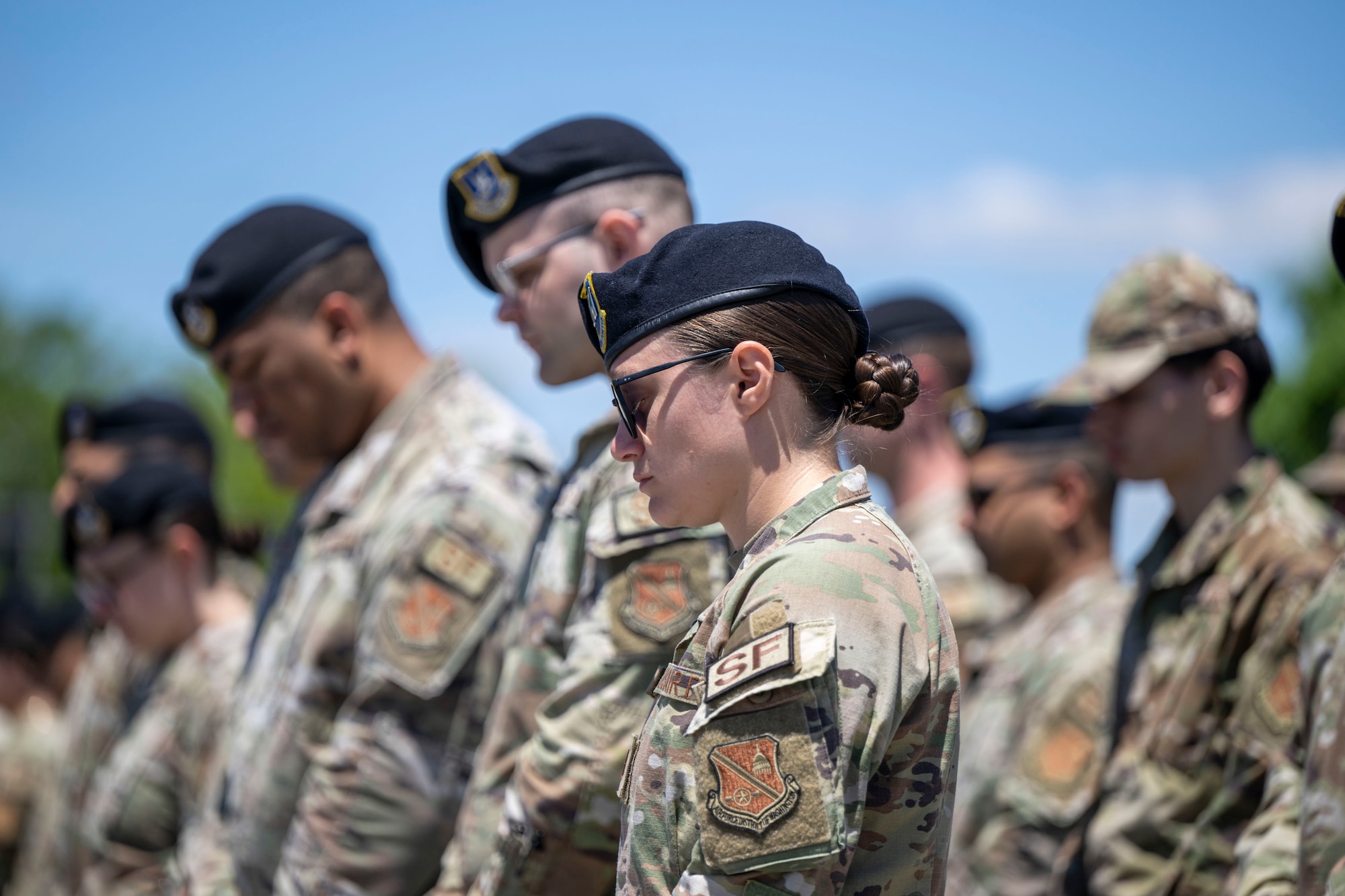 An Airman wearing a black beret facing left bows her head with others behind her doing the same.