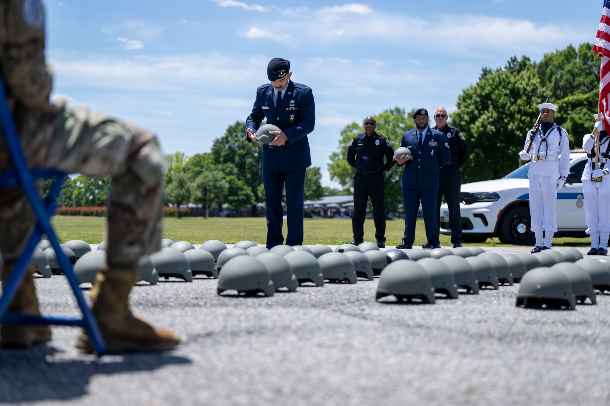 An Airman holds a helmet while standing among lines of helmets under a bright sky.