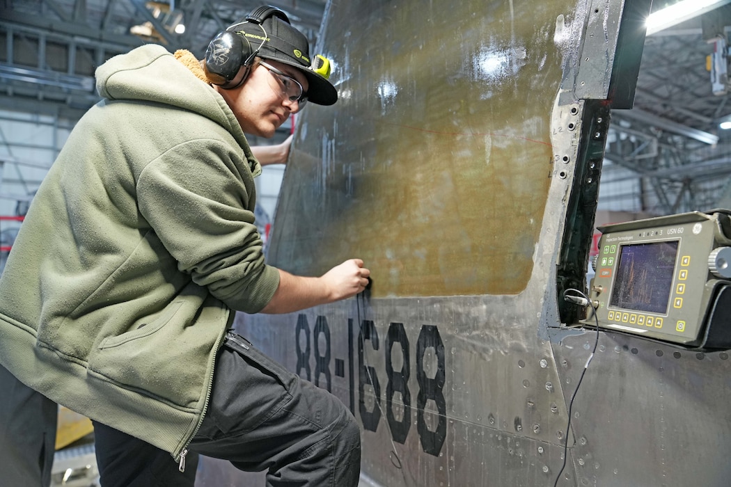 Photo shows a man using instruments to perform a test on the side of an aircraft.