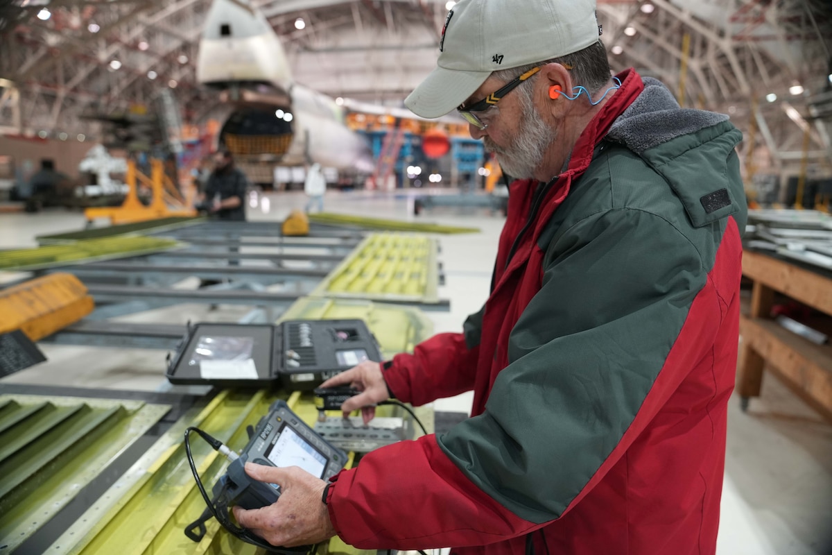 Photo shows man using machine to perform measurements on pieces of metal.