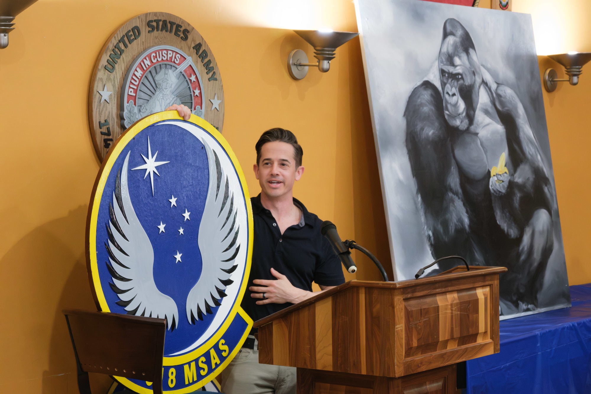 A man stands at a podium holding a large, colorful emblem for the 8th Mobility Support Advisory Squadron (8 MSAS).