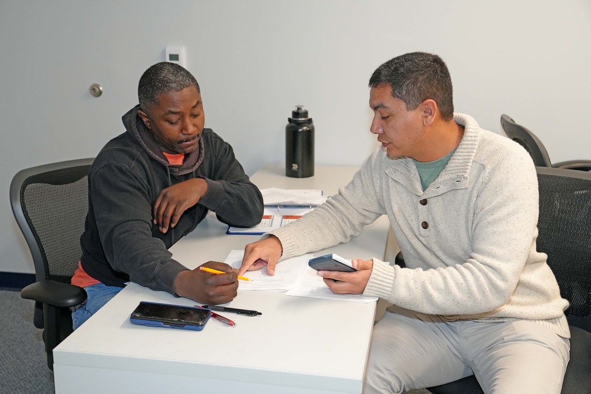Photo shows two men working around a table while reviewing papers.