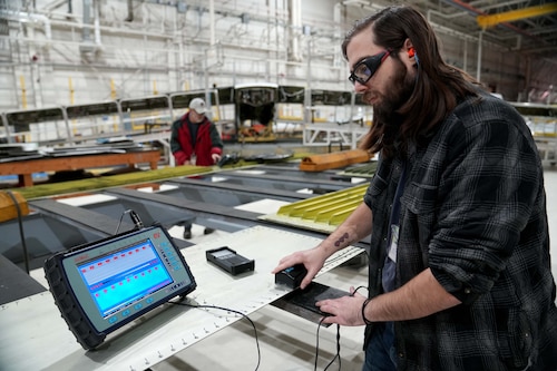 Photo shows man using a small machine on a piece of metal.