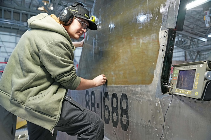 Photo shows a man using instruments to perform a test on the side of an aircraft.