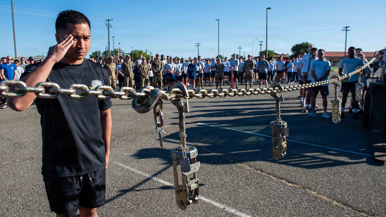 Airman salutes tie down hooks hanging during memorial ceremony