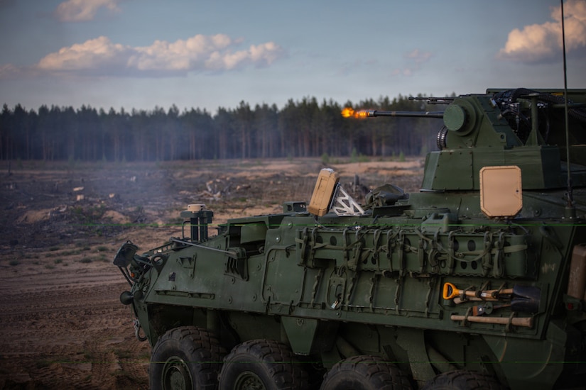 A military cannon fires a shot into a clearing surrounded by a wooded area.