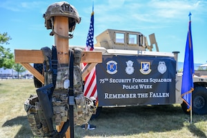 A combat cross and a banner reading, “75th Security Forces Squadron Police Week Remember the Fallen,” are displaye