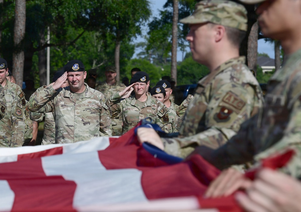 A group of people in U.S. Air Force uniforms render a salute behind a U.S. Flag.