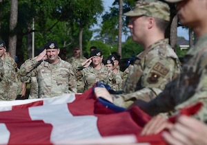 A group of people in U.S. Air Force uniforms render a salute behind a U.S. Flag.