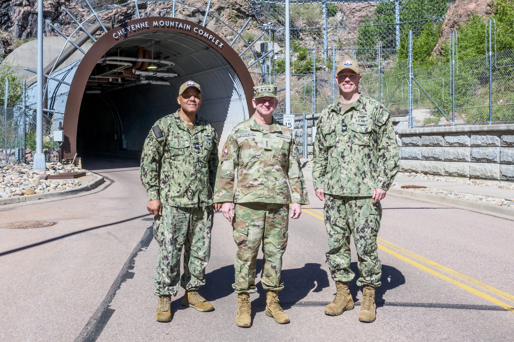 Three uniformed men stand in front of the large entrance to MWC carved into the side of a mountain