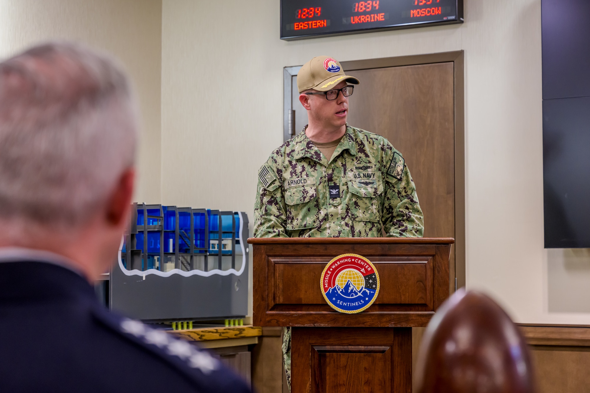 A uniformed man speaks from a wooden podium with the MWC logo on it