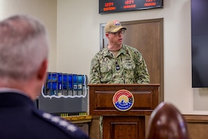 A uniformed man speaks from a wooden podium with the MWC logo on it
