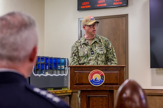 A uniformed man speaks from a wooden podium with the MWC logo on it