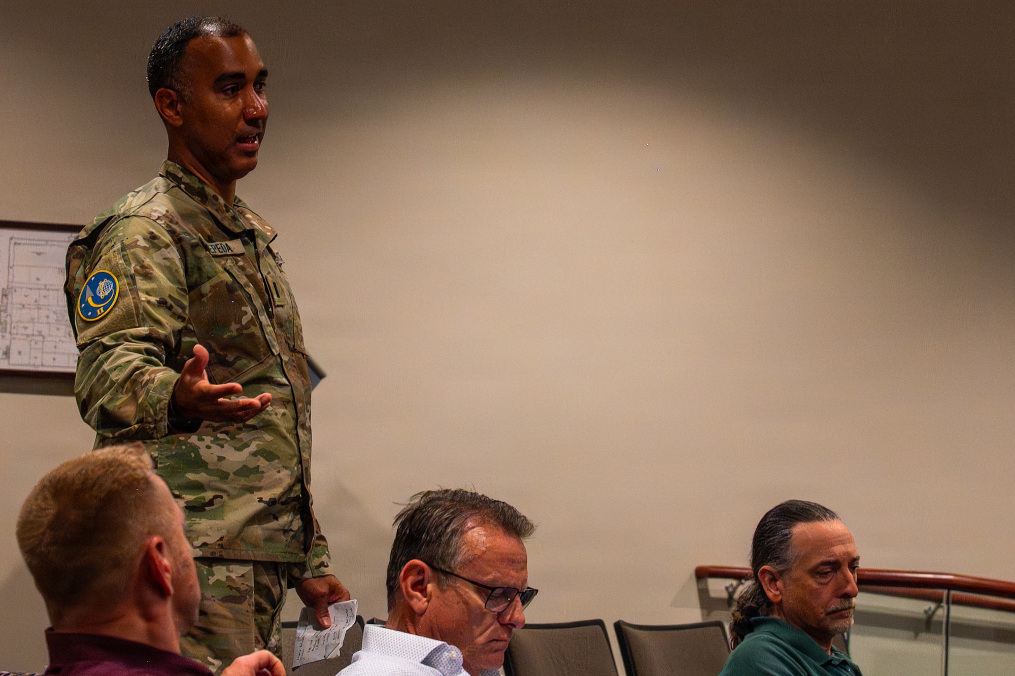 A person stands and asks a question inside an auditorium behind three people sitting down.