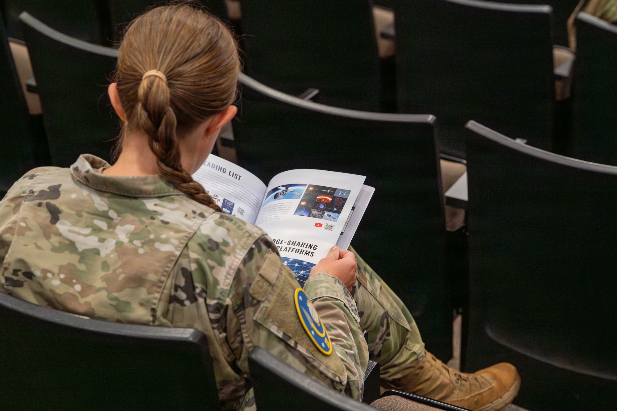 A person sits down in an auditorium seat and flips through pages of an informational journal.