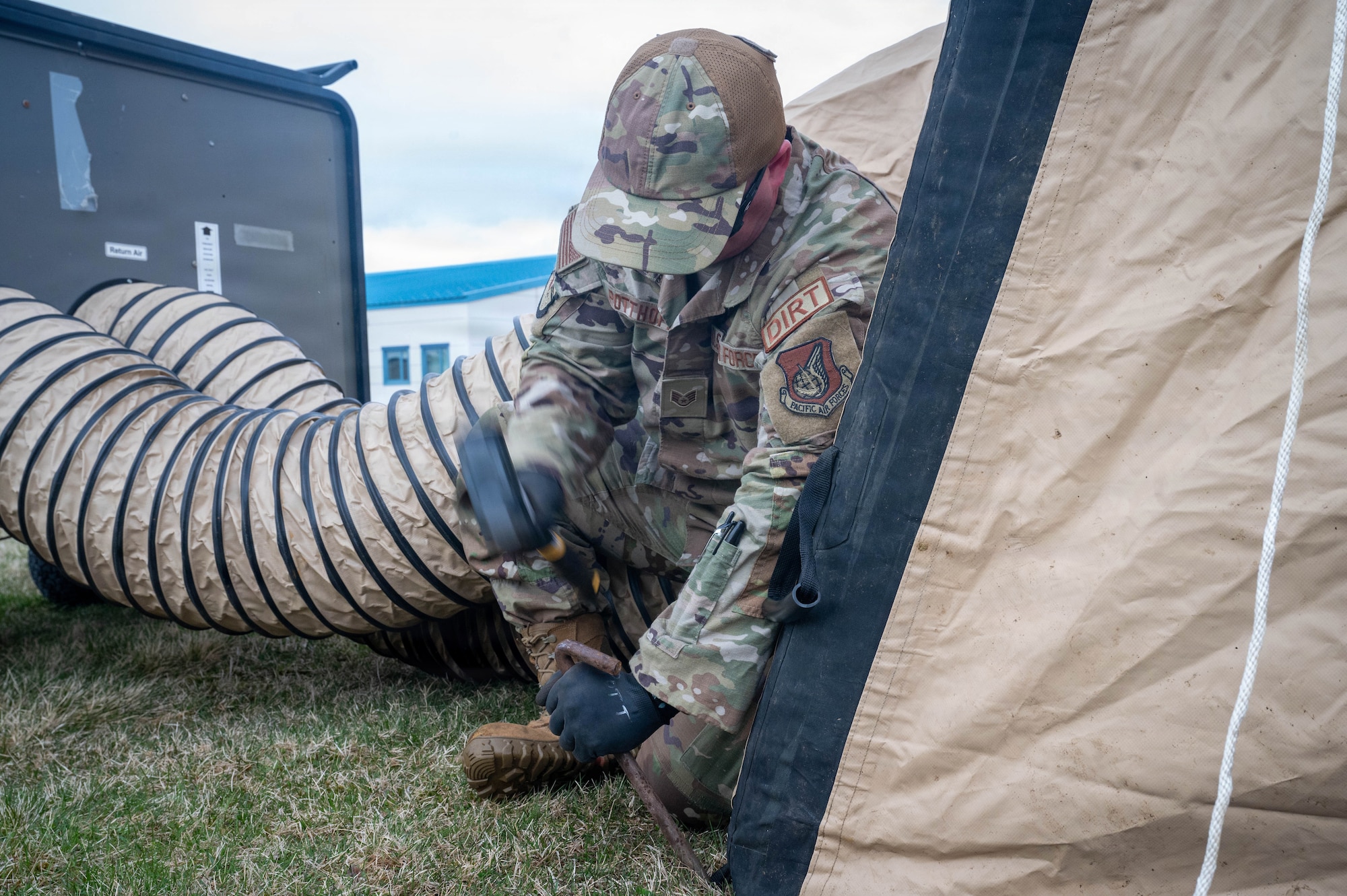 U.S. Air Force Staff Sgt. Gage Pottoff, 773d Civil Engineer Squadron pavements and construction equipment specialist, hammers a stake to hold down a tent during exercise Tropic Tundra 26 at Coast Guard Air Station Kodiak, Alaska, May 11, 2026.