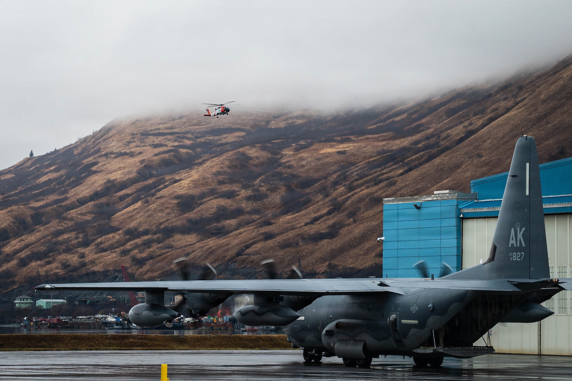 A U.S. Air Force C-130J Super Hercules aircraft assigned to the Alaska Air National Guard prepares for taxi and takeoff while a U.S. Coast Guard MH-60T Jayhawk flies overhead during exercise Tropic Tundra 26 at Coast Guard Air Station Kodiak, Alaska, May 11, 2026.