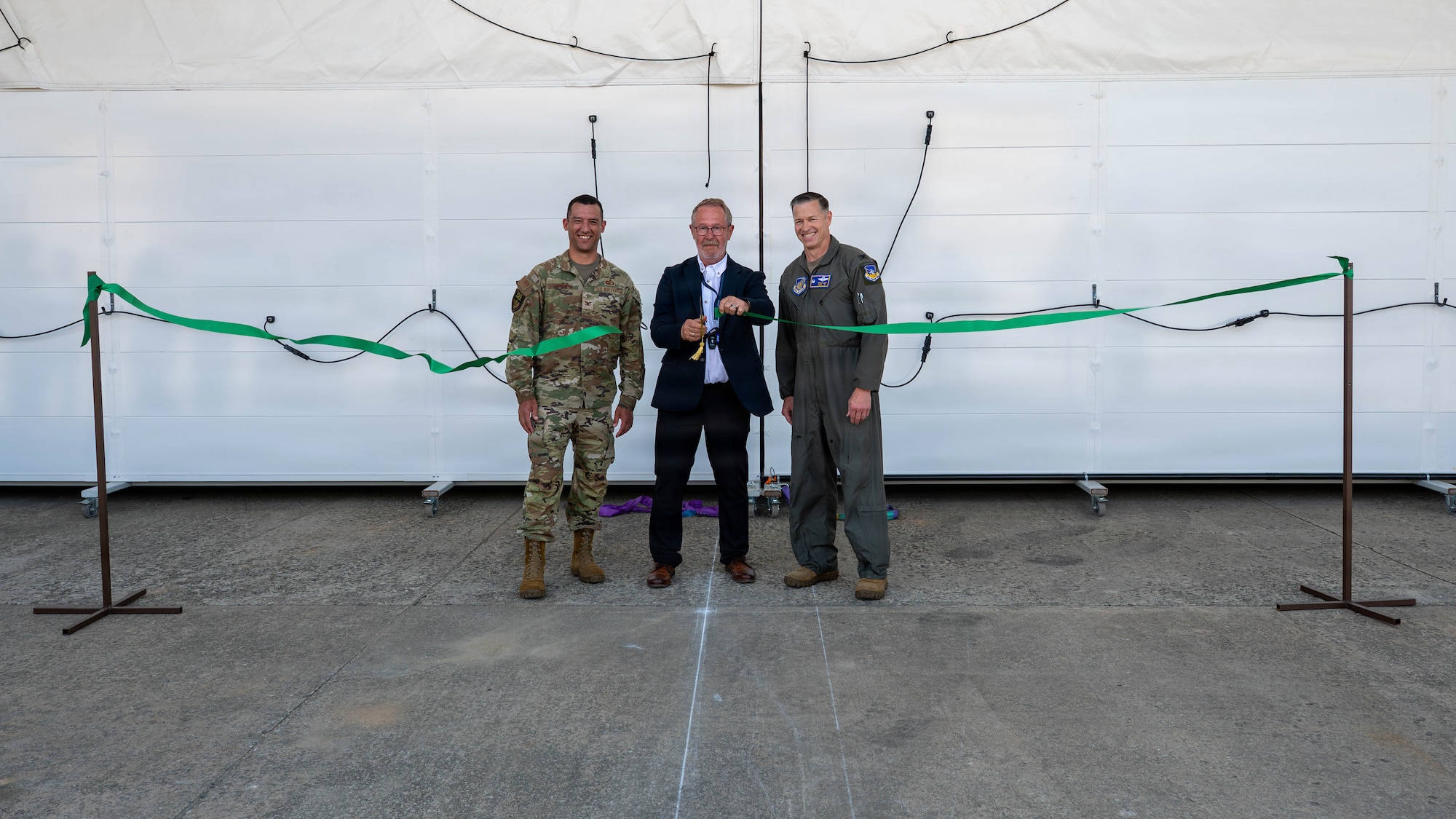 U.S. Air Force Col. Ryan Ley, right, 51st Fighter Wing commander, Anders Roberthson, center, construction site manager, and Col. Todd Dawson, left, Air Force Life Cycle Management Center Rapid Sustainment Office deputy division chief, cut a ribbon during a ceremony for a new deployable corrosion prevention and control facility at Osan Air Base, Republic of Korea, May 18, 2026. The facility supports combat readiness by enabling corrosion control operations to be completed on station rather than at off-site locations. (U.S. Air Force photo by Airman 1st Class Megan Cusmano)