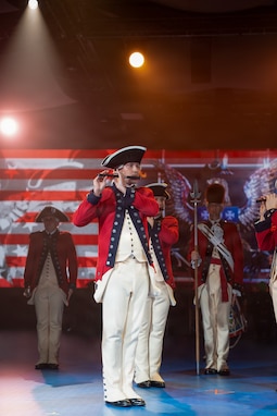 A Army Soldiers dressed in Revolutionary War-era uniforms are performing on fife, and other similarly dressed Soldiers are standing in the background.