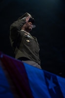 An Army general officer dressed in the Army green service dress uniform is saluting during am indoor public event.