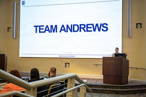 Person giving a lecture next to a screen that states "TEAM ANDREWS".