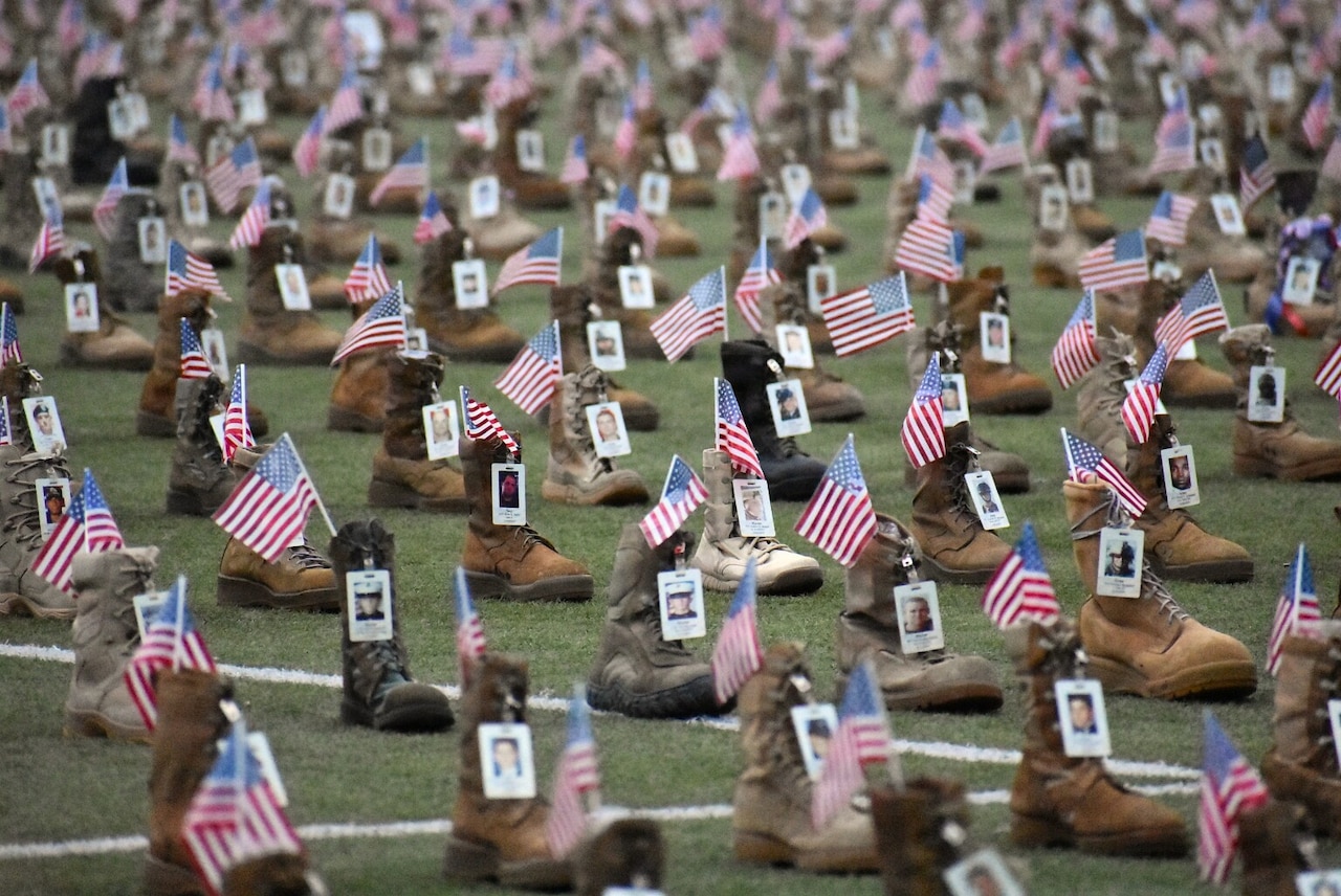 More than 7,500 combat boots are displayed on a field with small American flags and pictures of people attached to them.