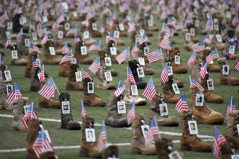 More than 7,500 combat boots are displayed on a field with small American flags and pictures of people attached to them.