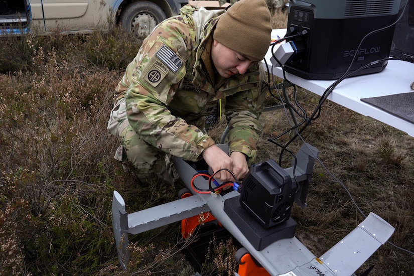 A man wearing camouflage military uniform works on a military drone.