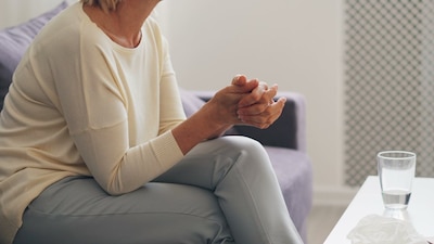 Women sitting on a couch with her hands clasped and her legs crossed.