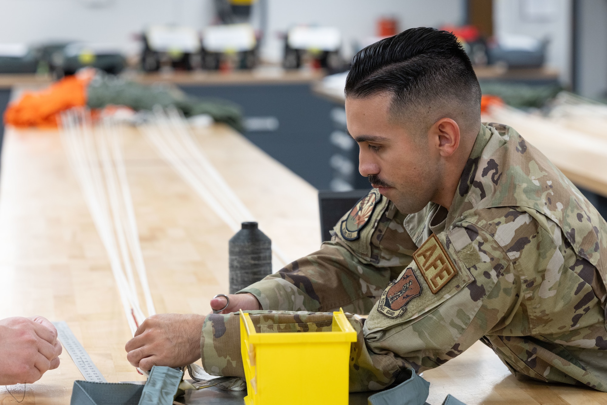 U.S. Air National Guard Tech. Sgt. Samuel Leiva, 162nd Aircrew Flight Equipment noncommissioned officer in charge, demonstrates parachute setup at Morris Air National Guard Base, Ariz., May 1, 2026. The 162nd AFE flight secured two Navy-funded technician positions, facilitating parachute inspections for the Naval Air Station Fighter Weapons School program. (U.S. Air National Guard photo by Tech. Sgt. Hampton Stramler)