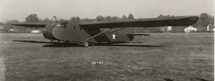 A black-and-white photo of a World War II-era glider sitting in a grassy field.