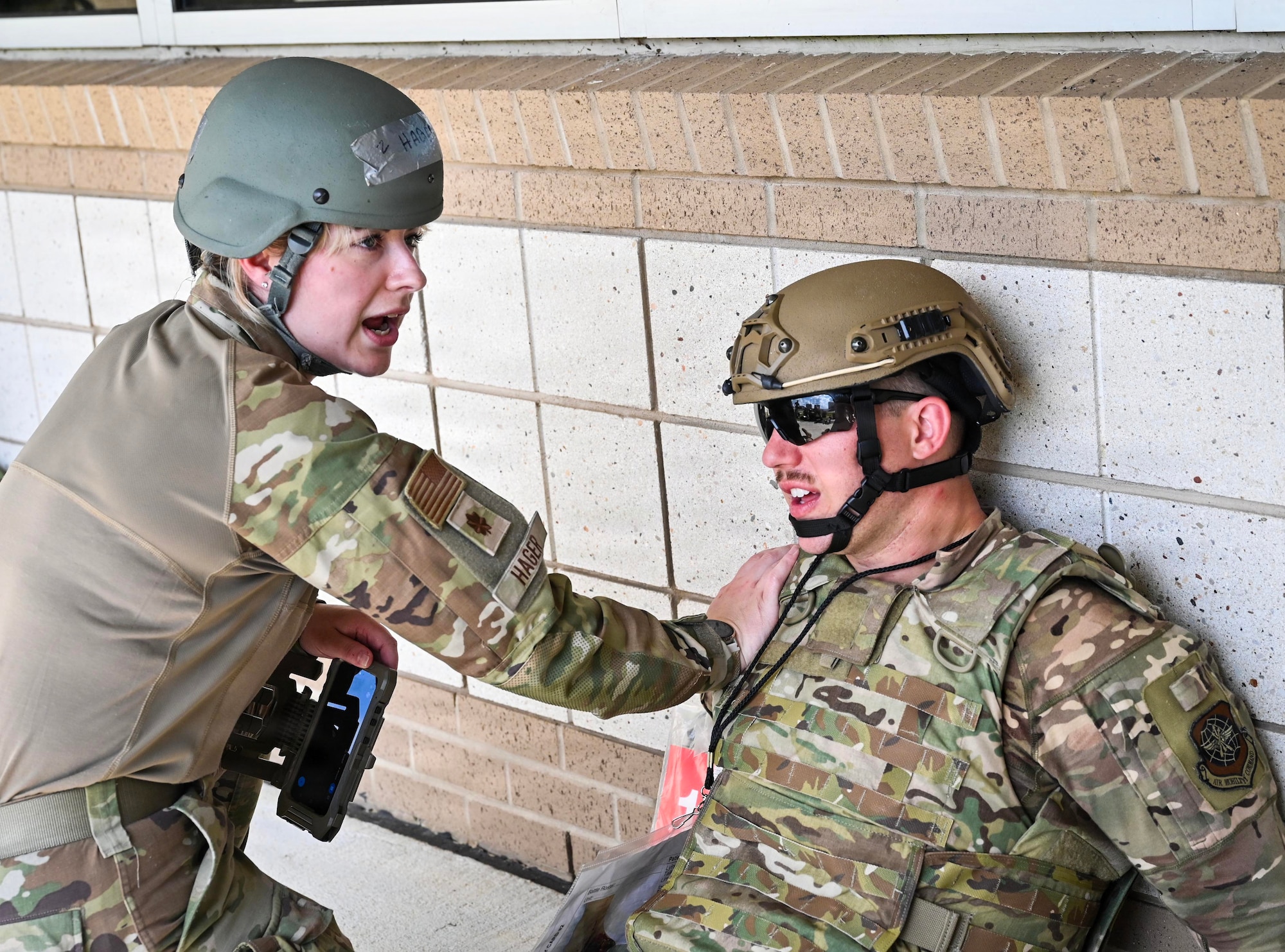 A woman in uniform has hand placed on man in uniform sitting on the ground.