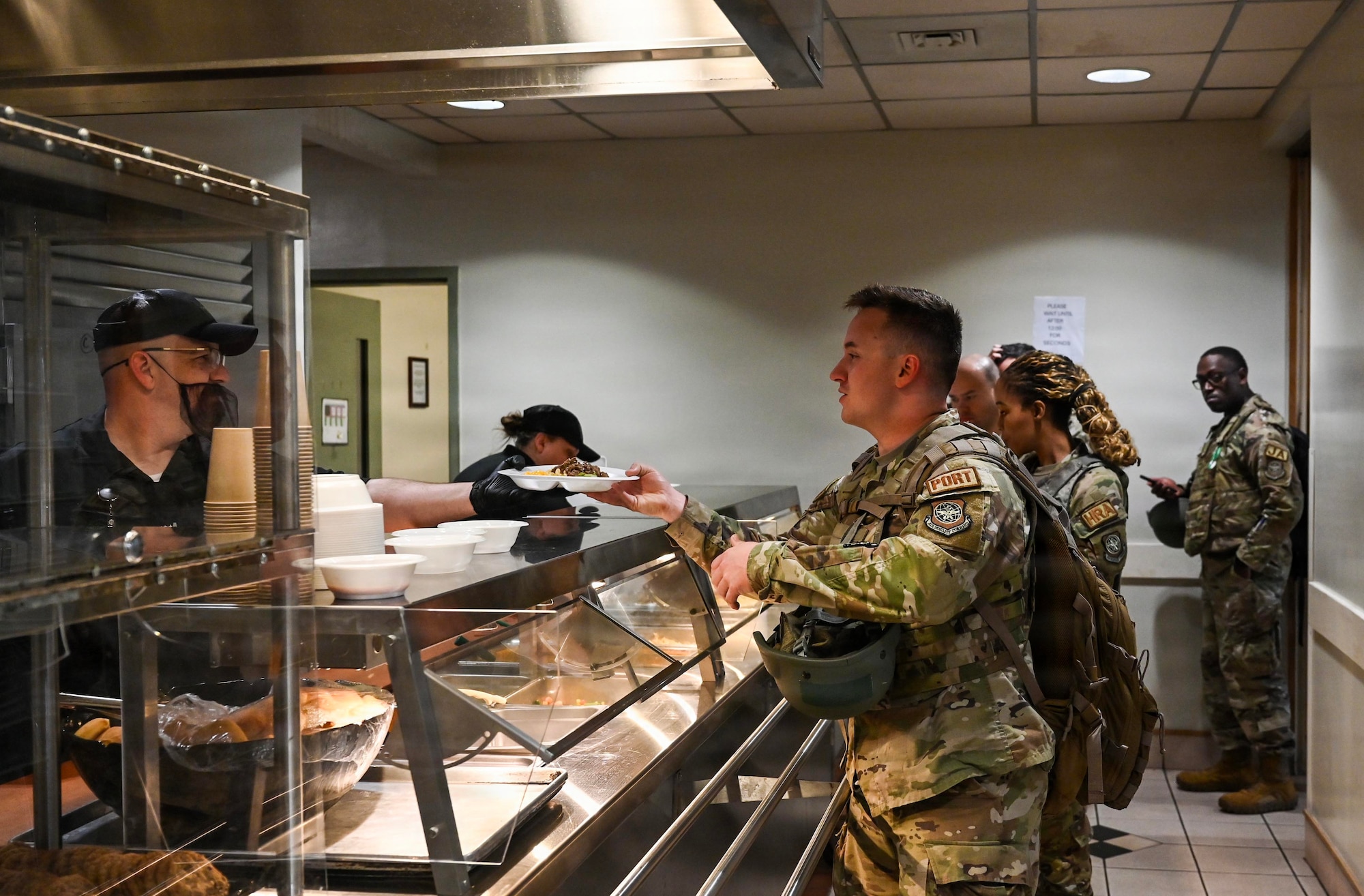 Military members receive food in a cafeteria line.