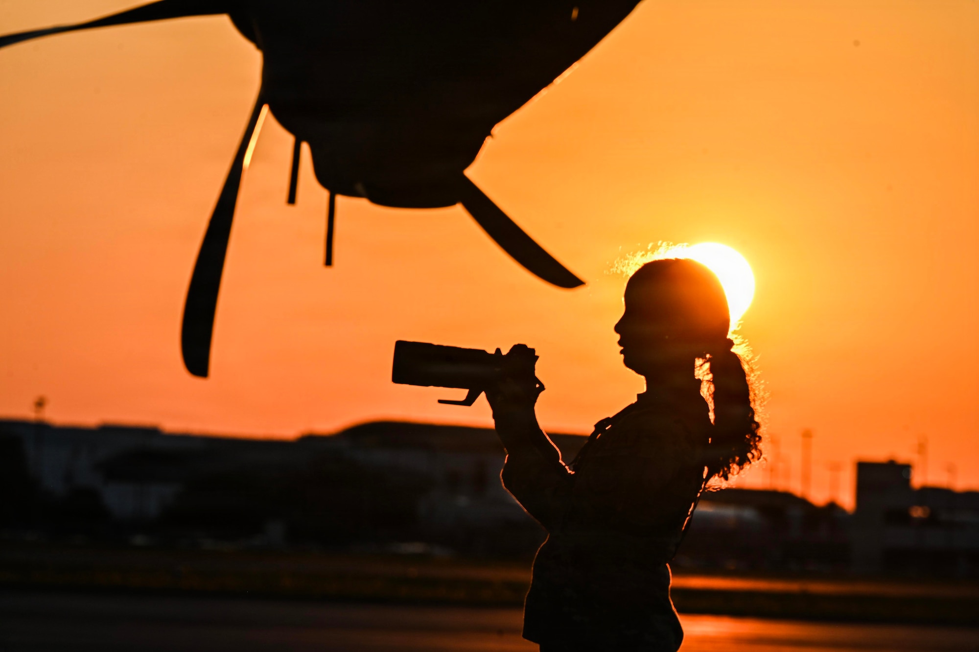 Silhouette of a woman using a camera under an aircraft propeller.