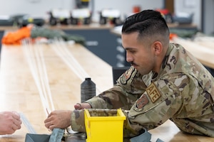 U.S. Air National Guard Tech. Sgt. Samuel Leiva, 162nd Aircrew Flight Equipment noncommissioned officer in charge, demonstrates parachute setup at Morris Air National Guard Base, Ariz., May 1, 2026. The 162nd AFE flight secured two Navy-funded technician positions, facilitating parachute inspections for the Naval Air Station Fighter Weapons School program. (U.S. Air National Guard photo by Tech. Sgt. Hampton Stramler)