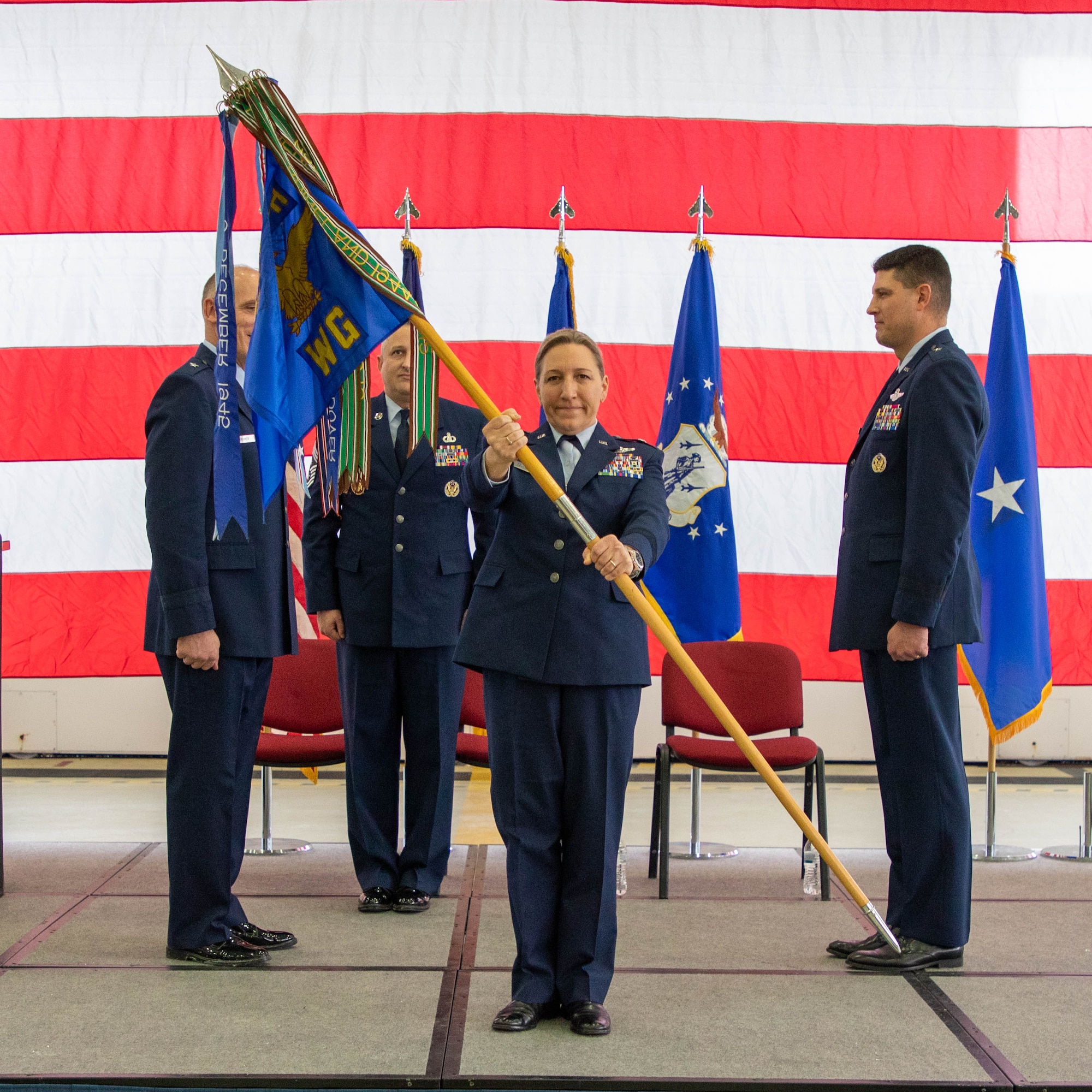 Female air force officer in dress blue uniform presenting 127th Wing guidon to the audience on stage