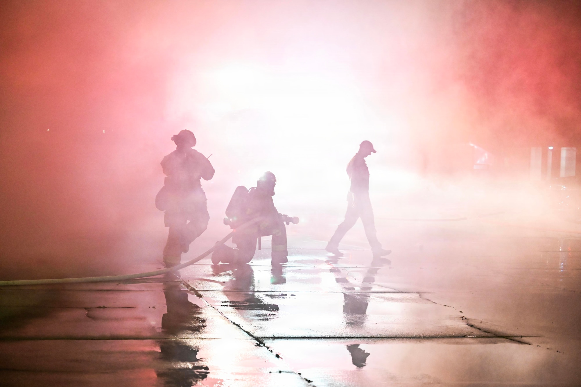 Three firefighters use hose to spray water.
