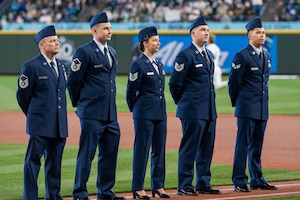 Five people stand shoulder to shoulder on a baseball field.