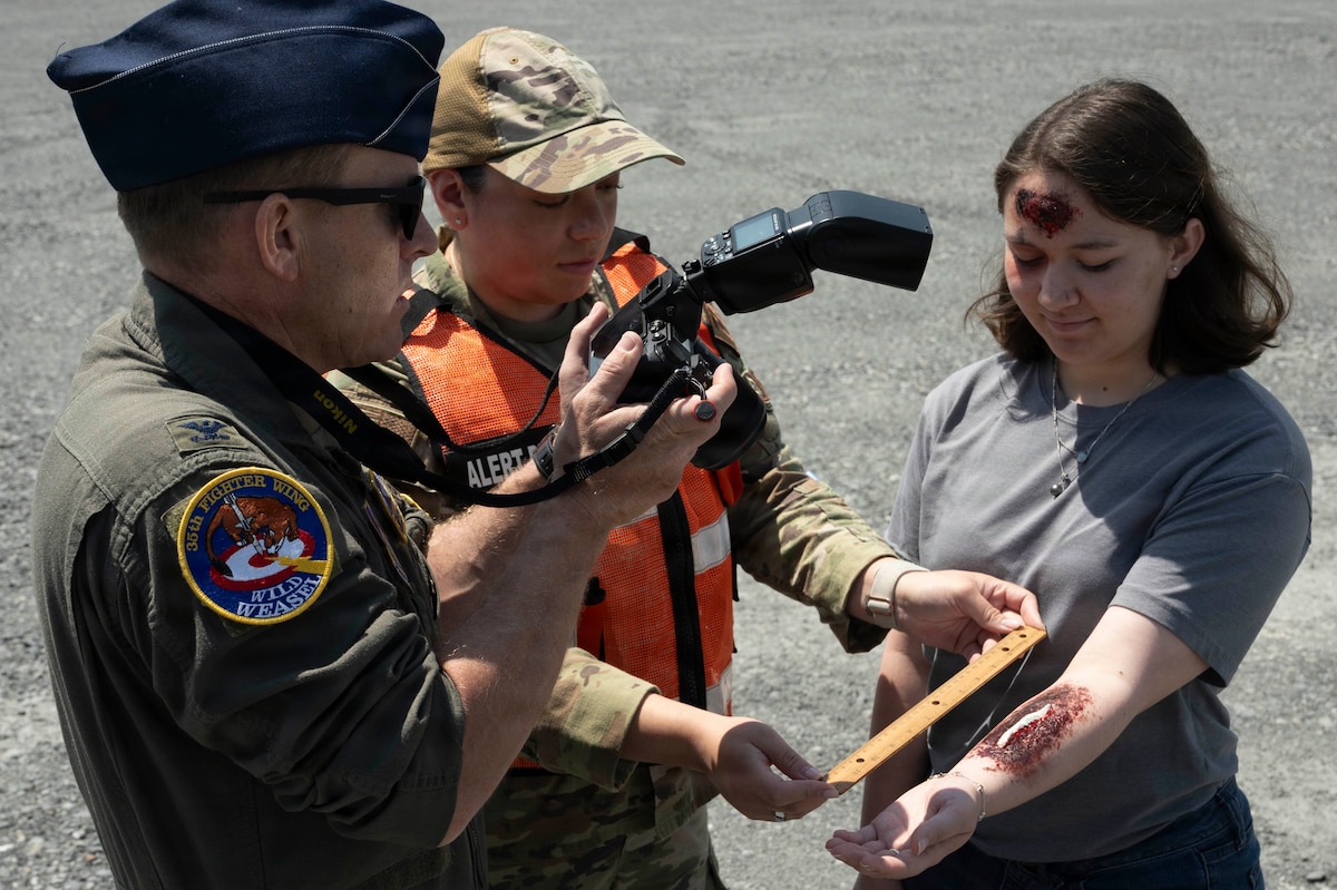 U.S. Air Force Col. Paul Davidson, 35th Fighter Wing commander, Airman 1st Class Jessel Fabara, Airman 1st Class Hannah Bench, both 35th FW Public Affairs specialists, conduct a simulated alert photo event during a Wild Weasel Walk-through of the 35th FW public affairs unit at Misawa Air Base, Japan, May 18, 2026. (U.S. Air Force photo by Senior Airman Gavin Hameed)