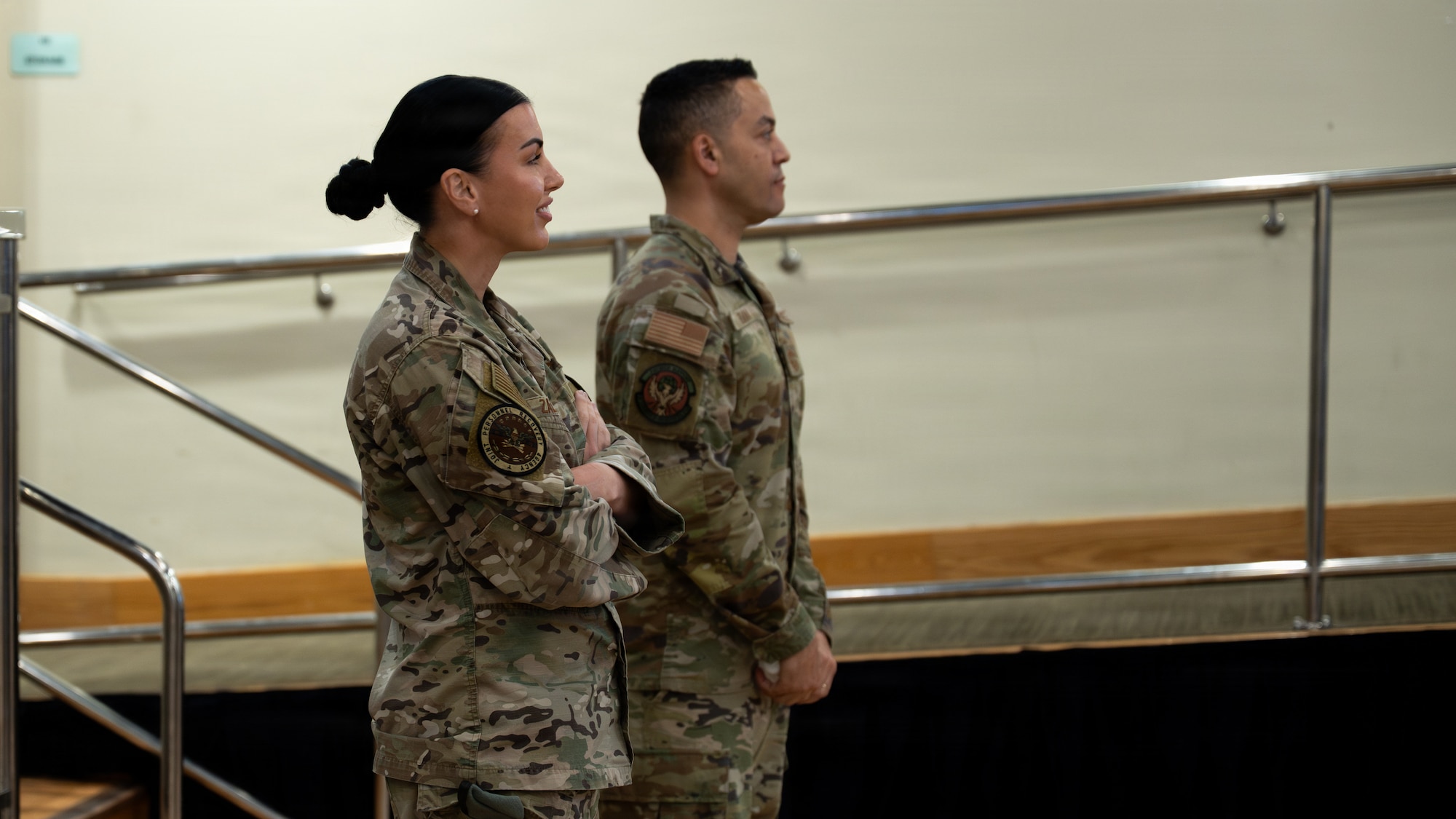 Two people, a man and a woman, wearing OCP camouflage uniforms look off to the side