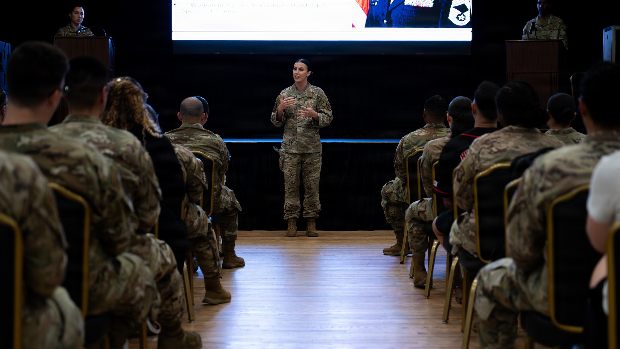 Woman in OCP camouflage uniform speaks in front of an audience