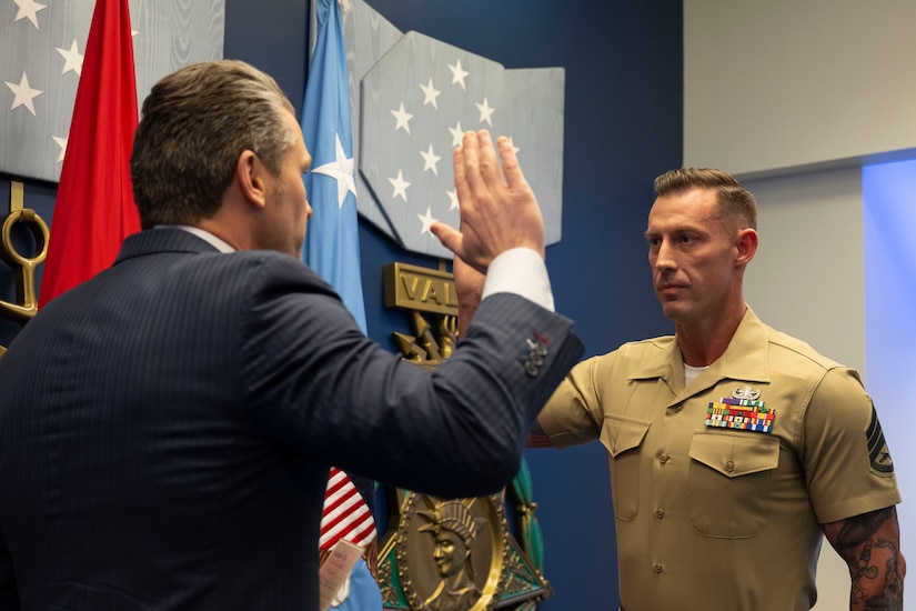 Secretary of War Pete Hegseth and a Marine face each other in a room, each holding up their right hands.
