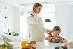 Pregnant woman standing at a kitchen counter while holding a child's ponytail.