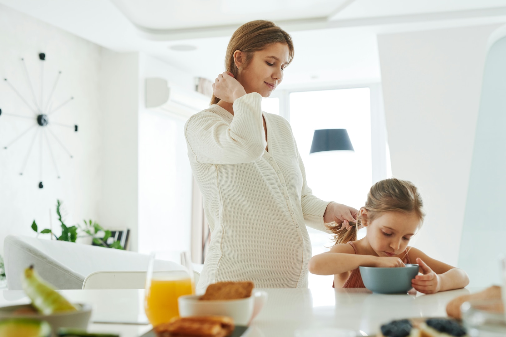 Pregnant woman standing at a kitchen counter while holding a child's ponytail.