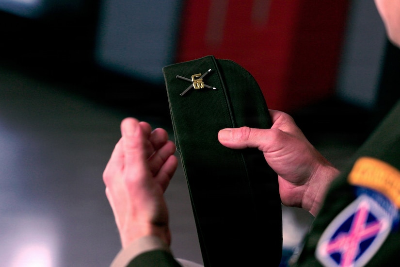 A person holds a military cap with an insignia on it.