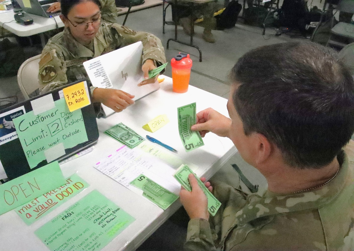 Photo shows two uniformed individuals handling fake, paper money across from each other.