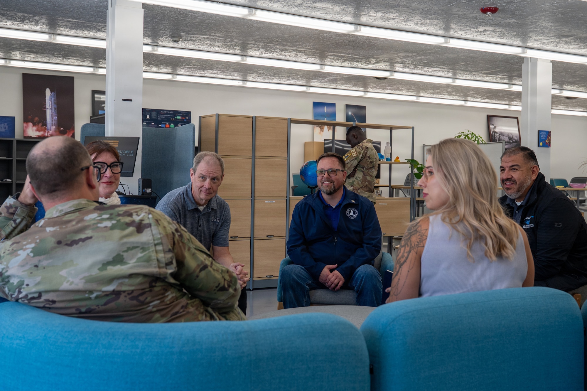 People sit on couches and chairs inside and talk during a group discussion.